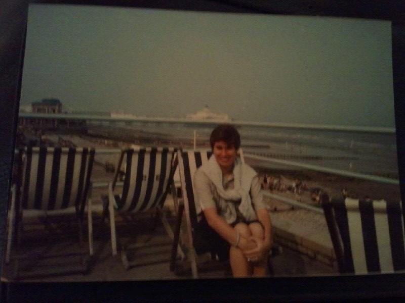 woman sitting on beach chair with brighton pier in background in 1980's