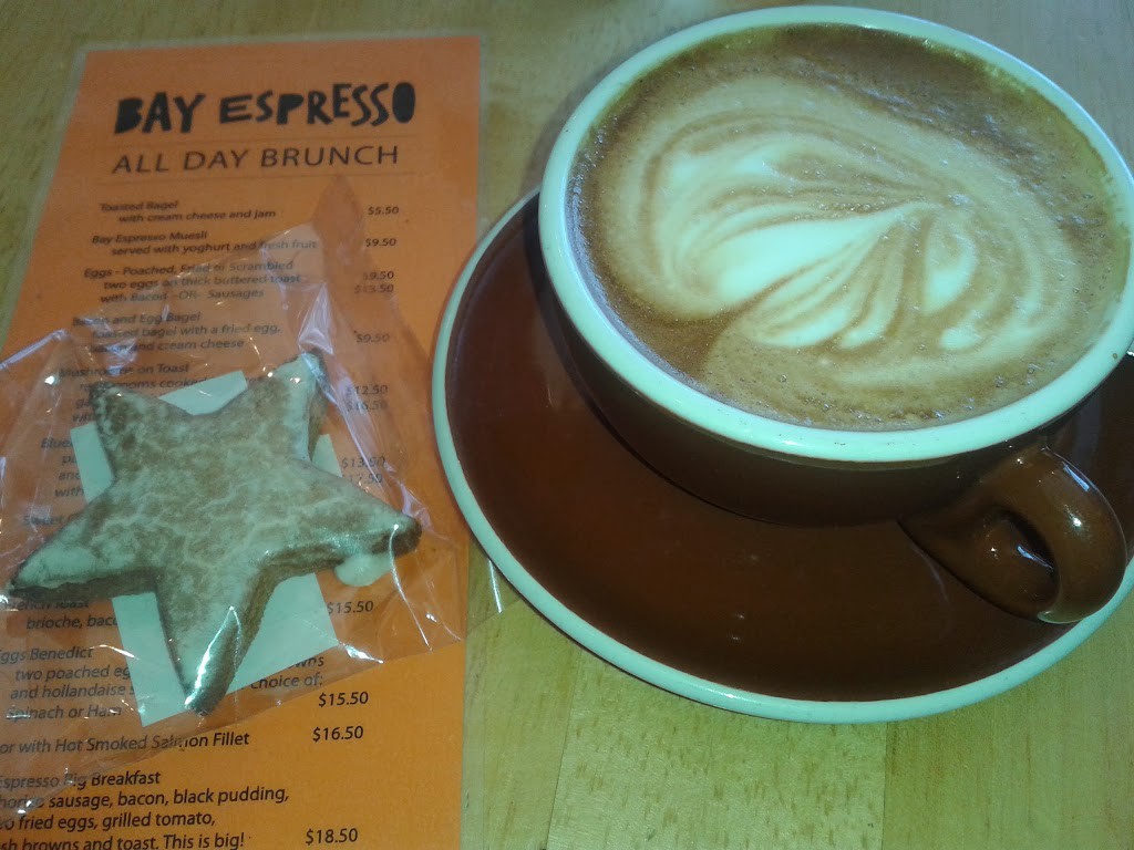 flat white coffee next to star shaped biscuit on top of orange menu with "bay espresso" at top