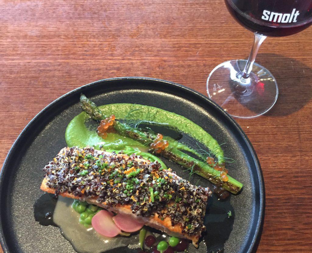 salmon dish on black plate with glass of red wine