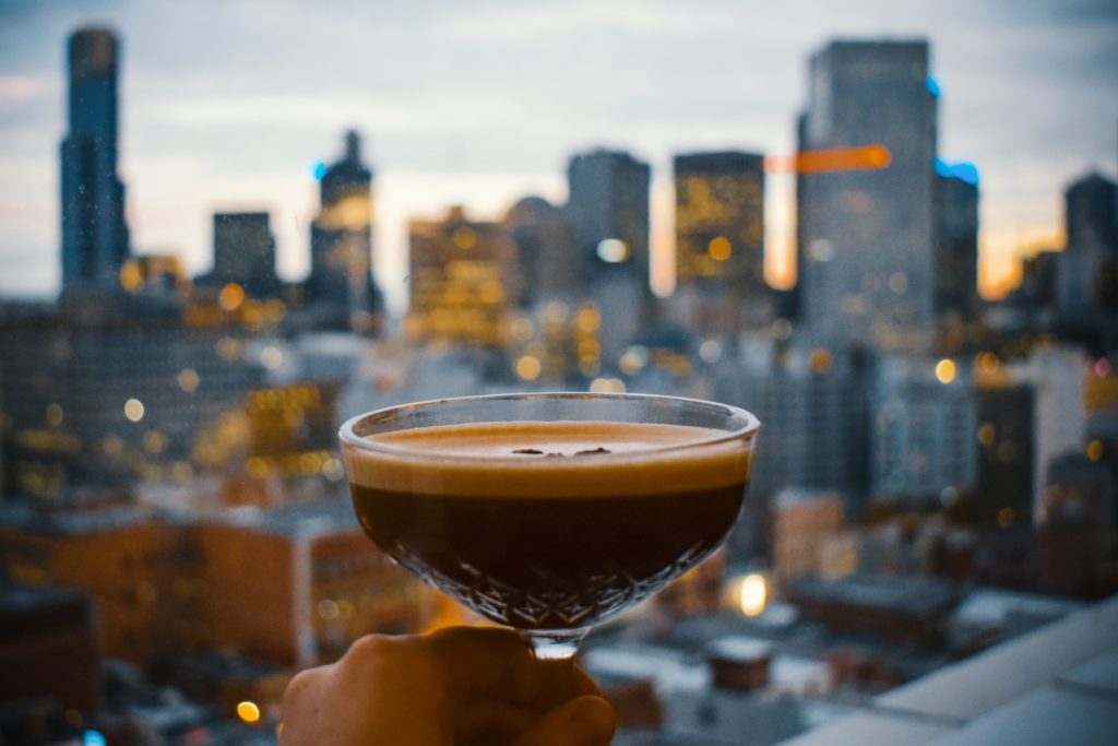 hand holding cocktail glass with city skyscrapers in background