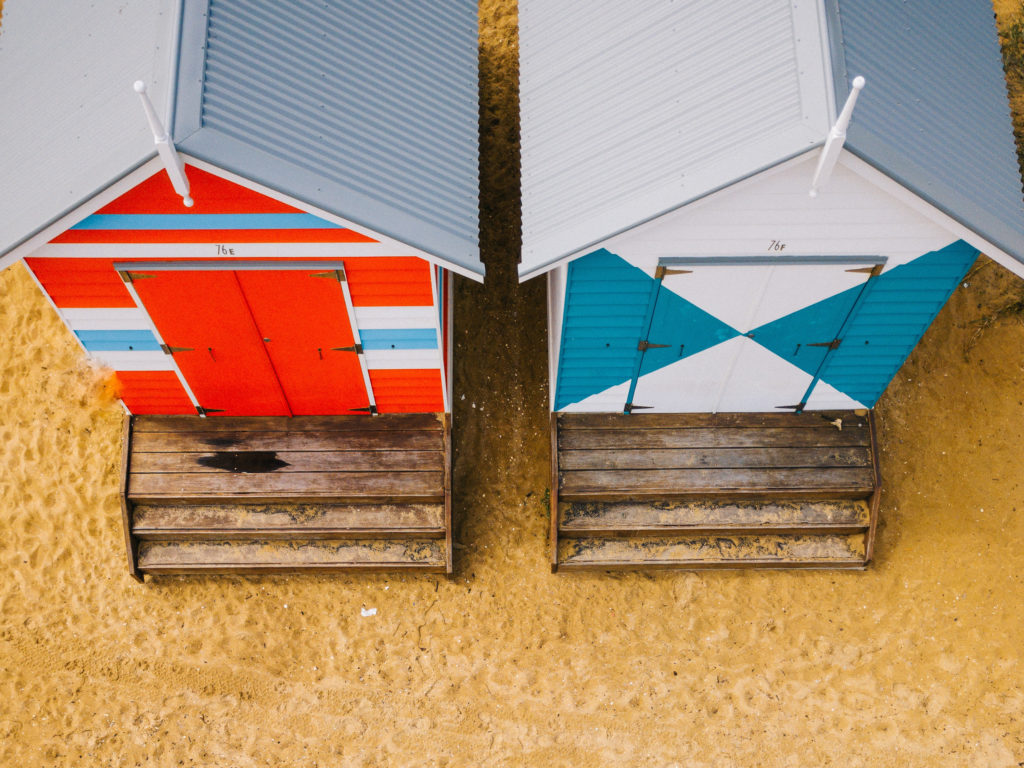 aerial photo of two blue and red wooden sheds on sand