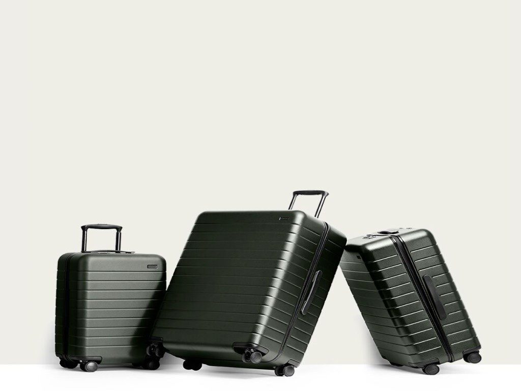 three hard black suitcases against a vanilla wall