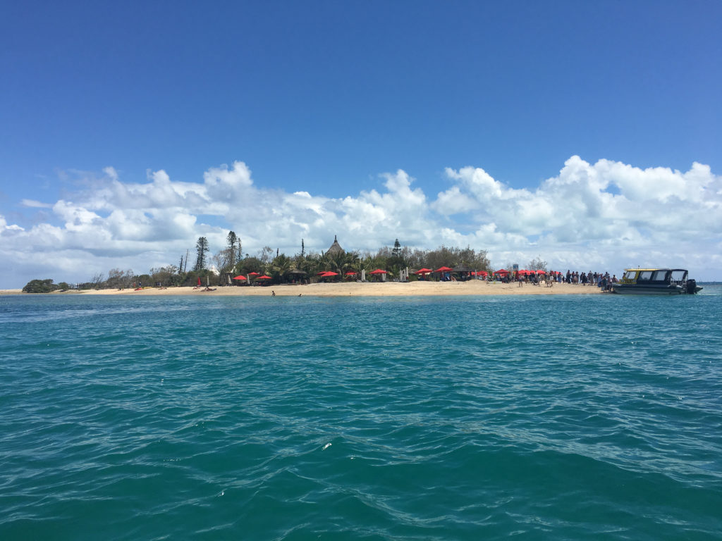 Small Island with red sun umbrellas from a distance in the ocean