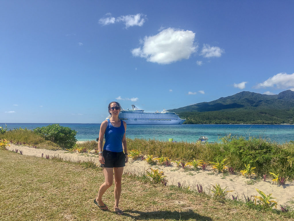 girl posing on green island in front of turquoise water and cruise ship