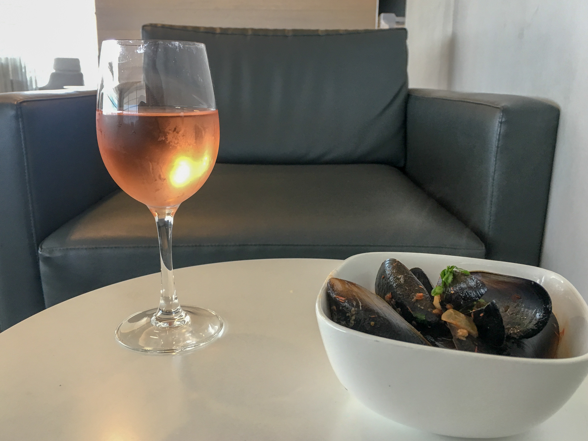 glass of wine and bowl of mussels on white table with grey armchair