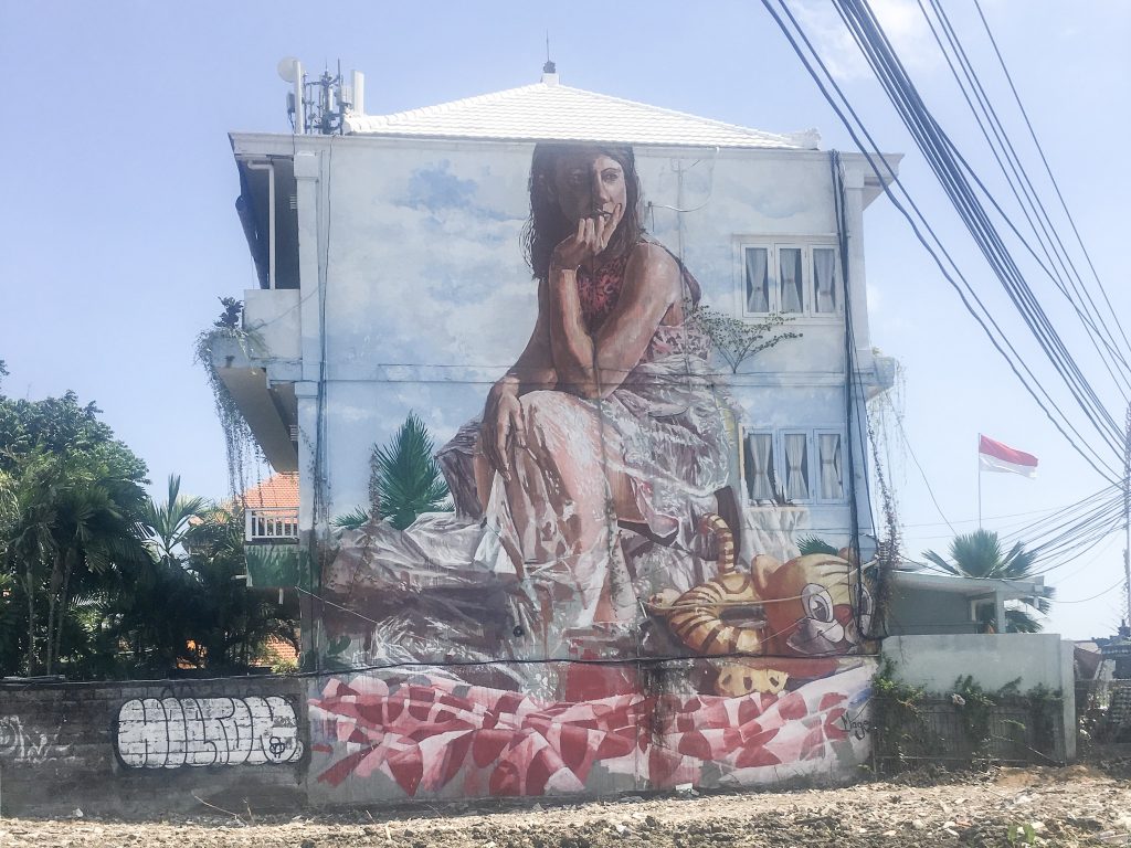 pained mural of girl sitting at beach on building wall