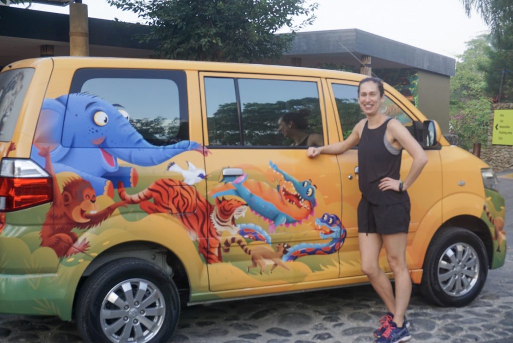 Young woman in black shorts and singlet next to yellow bali zoo branded vehicle