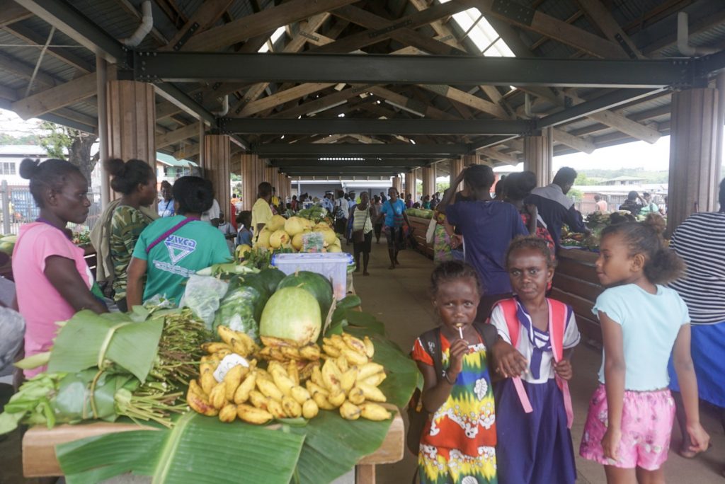 three young girls walking around fruit markets in pacific island town