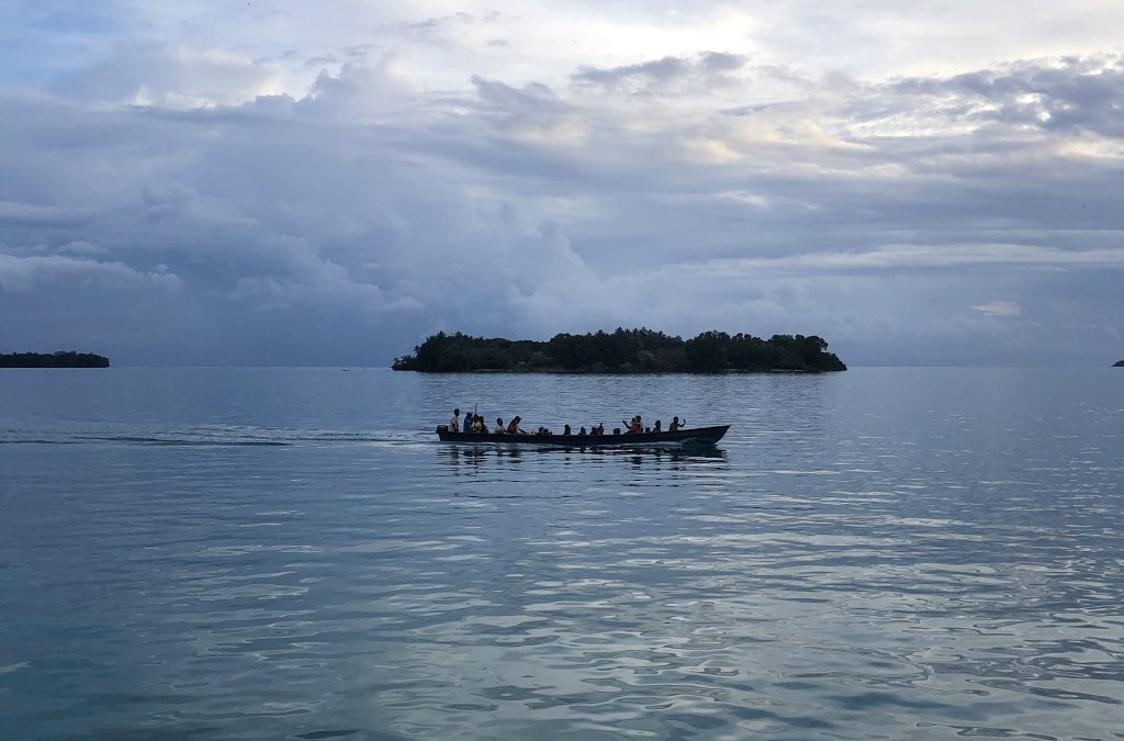 group of people in a small boat with two islands in background