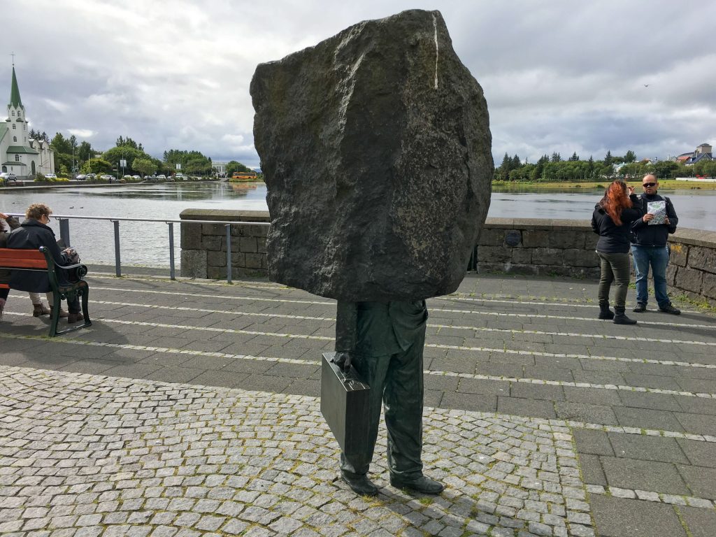 Statue of man holding briefcase with rock on his head on lake front in Reykjavik Iceland. Monument to the Unknown Bureaucrat.