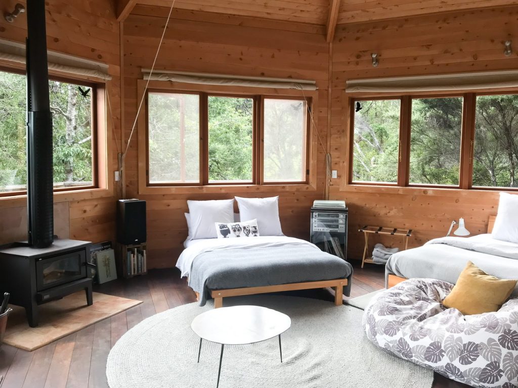 Interior of Away treehouse Waiheke Island accommodation with fire, two beds, bean bag and wooden paneled walls