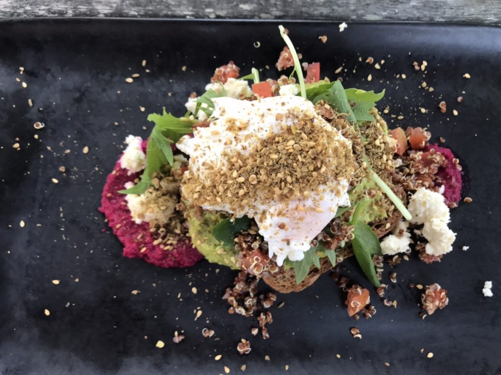 Smashed avocado on seeded sourdough with beetroot hummus, topped with a quinoa tomato salsa, feta, dukkah and a poached egg