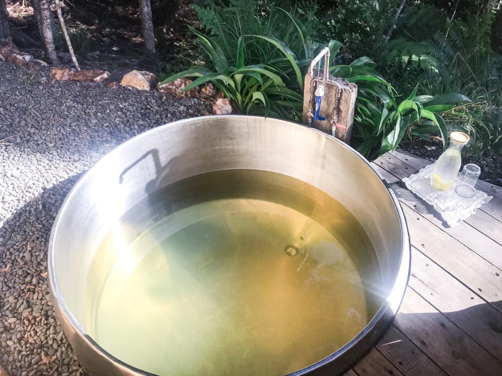 hot tub made from wine vat filled with yellowish spring water at bush edge