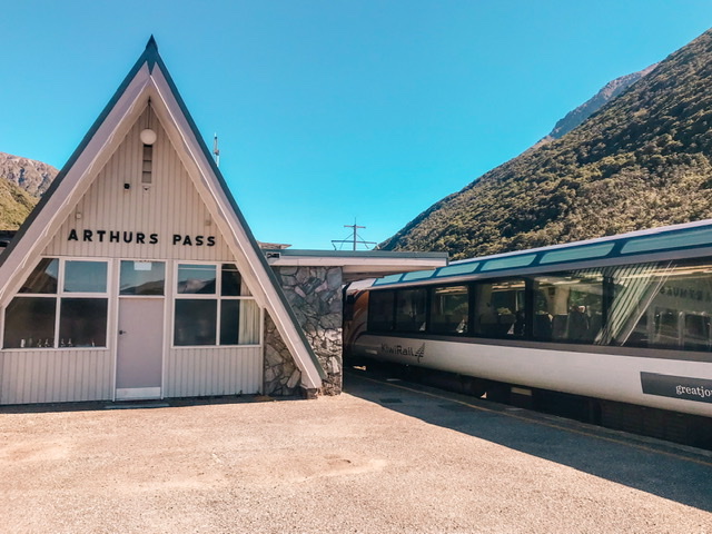 Triangular building with Arthurs Pass sign with train on platform to left