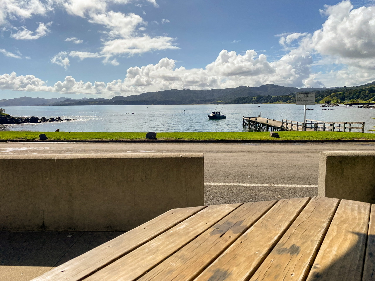 View across a road of Waihau Bay Wharf, Waihau Bay and a small boat coming in