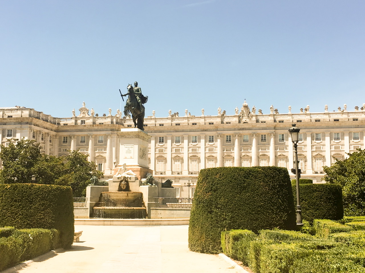 White Royal Palace building with statue and scultured green bushes in Madrid