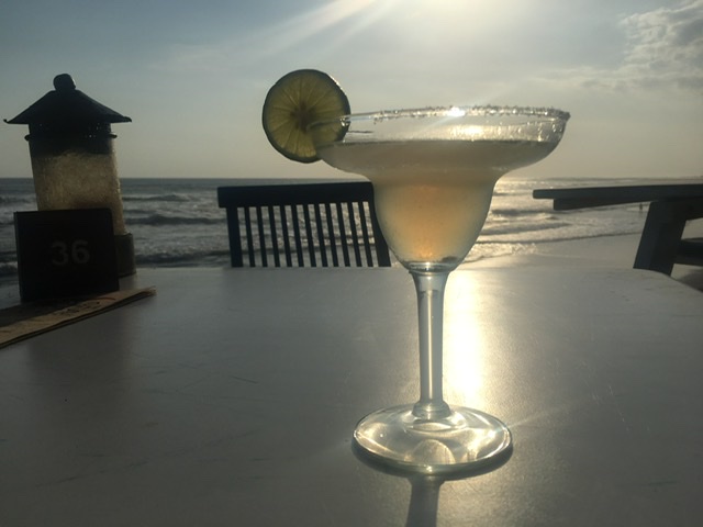 margarita cocktail with salt rim and lime wedge on table at beach at dusk