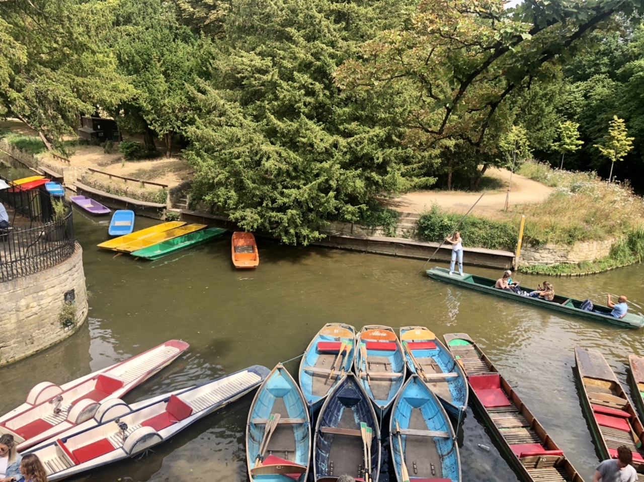 Group of four people punting in Oxford with numberous empty boats lined up along river edge
