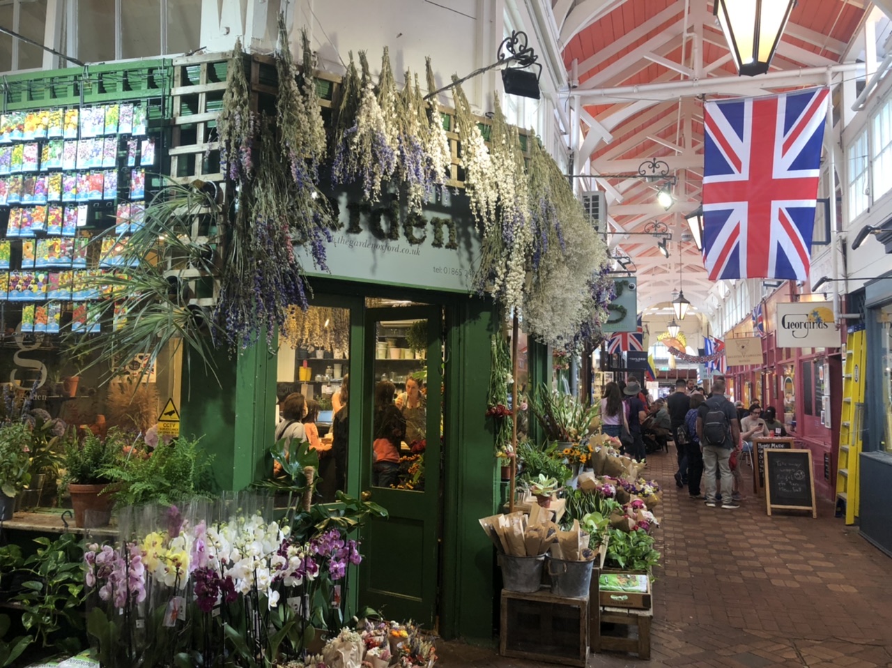 Garden centre on corner in Oxford Covered Market looking down row with shops and British flag hanging from ceiling