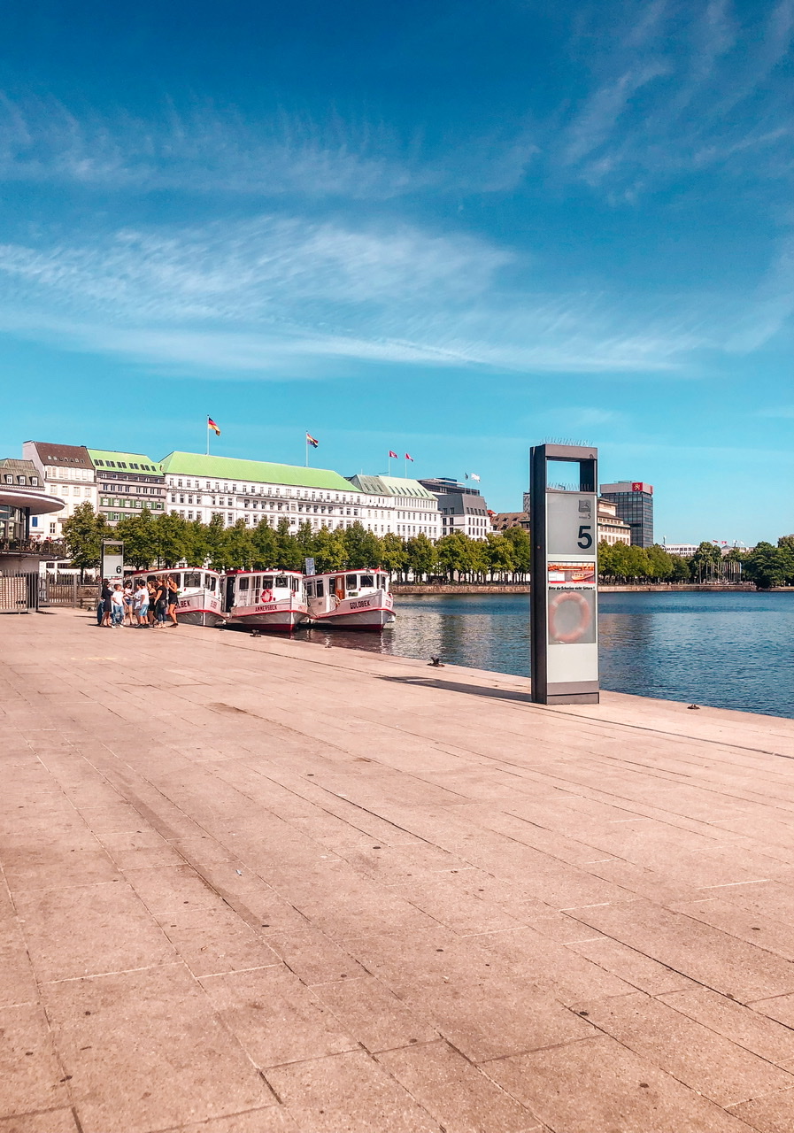 Binnenalster waterfront Hamburg with three small boats parked side by side at concrete edge with white buildings in background