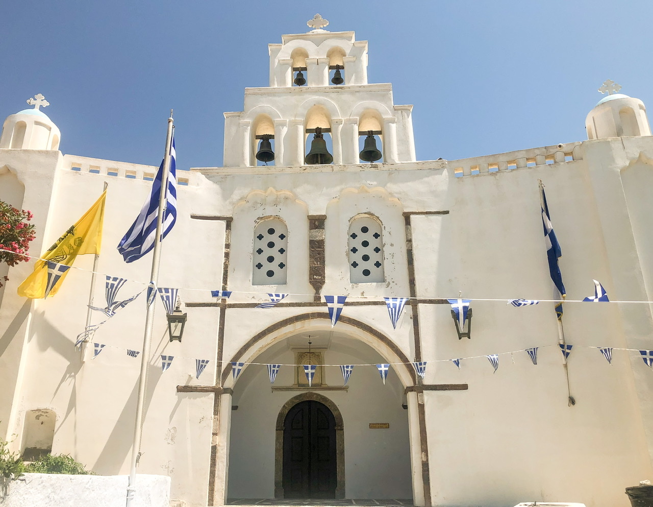 Exterior of church of white church Pyrgos Kallistis with five bells in tower on top centre in Santorini