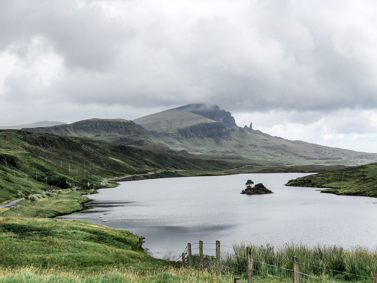 View of Old Man of Storr in distance with lake in front surrounded by greenery