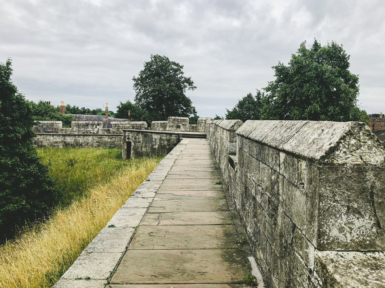 Paved footpath along the top of medieval city wall with green grass on left and wall on right
