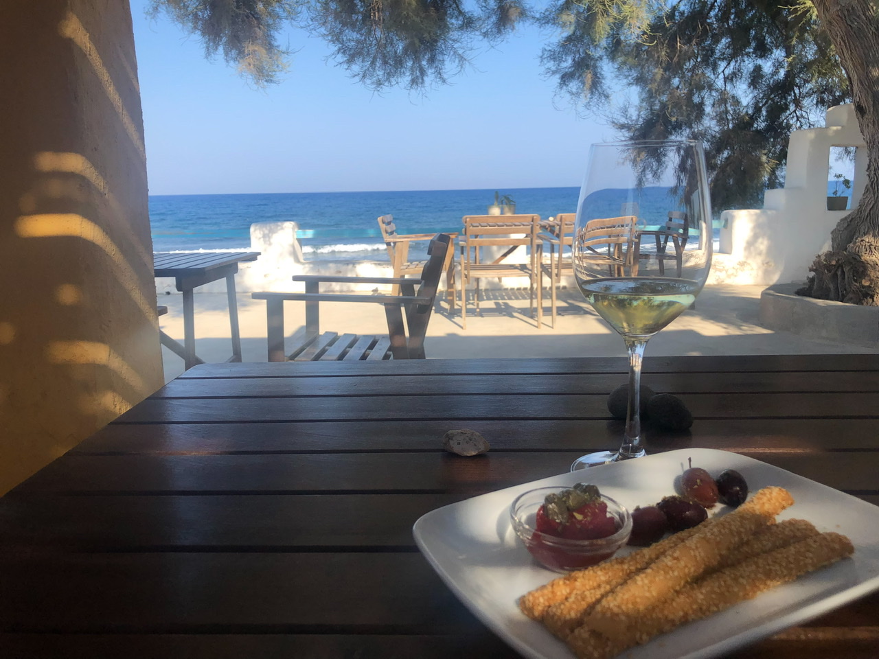 Plate of breadsticks and olives with tasting glass of white wine with ocean in background