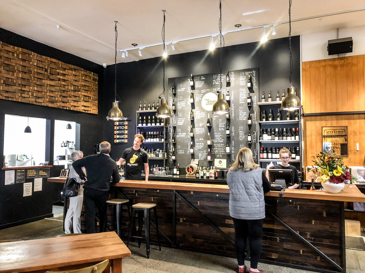 Industrial looking bar area at The Urban Winery Napier, two staff behind the bar serving three customers