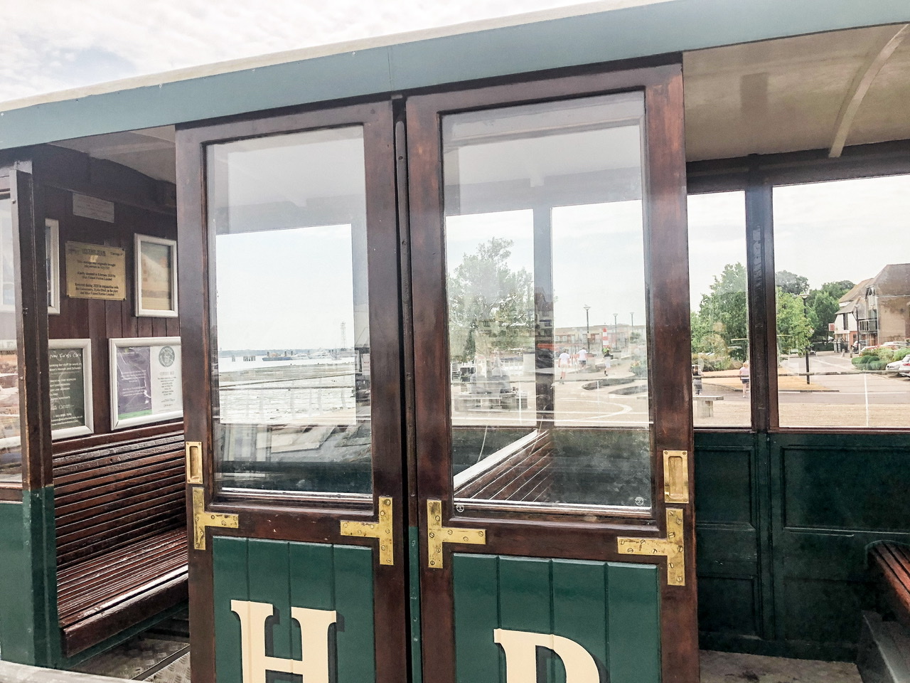 Looking into wooden Heritage train with green detailing and wooden bench seats, town of Hythe visible outside far window
