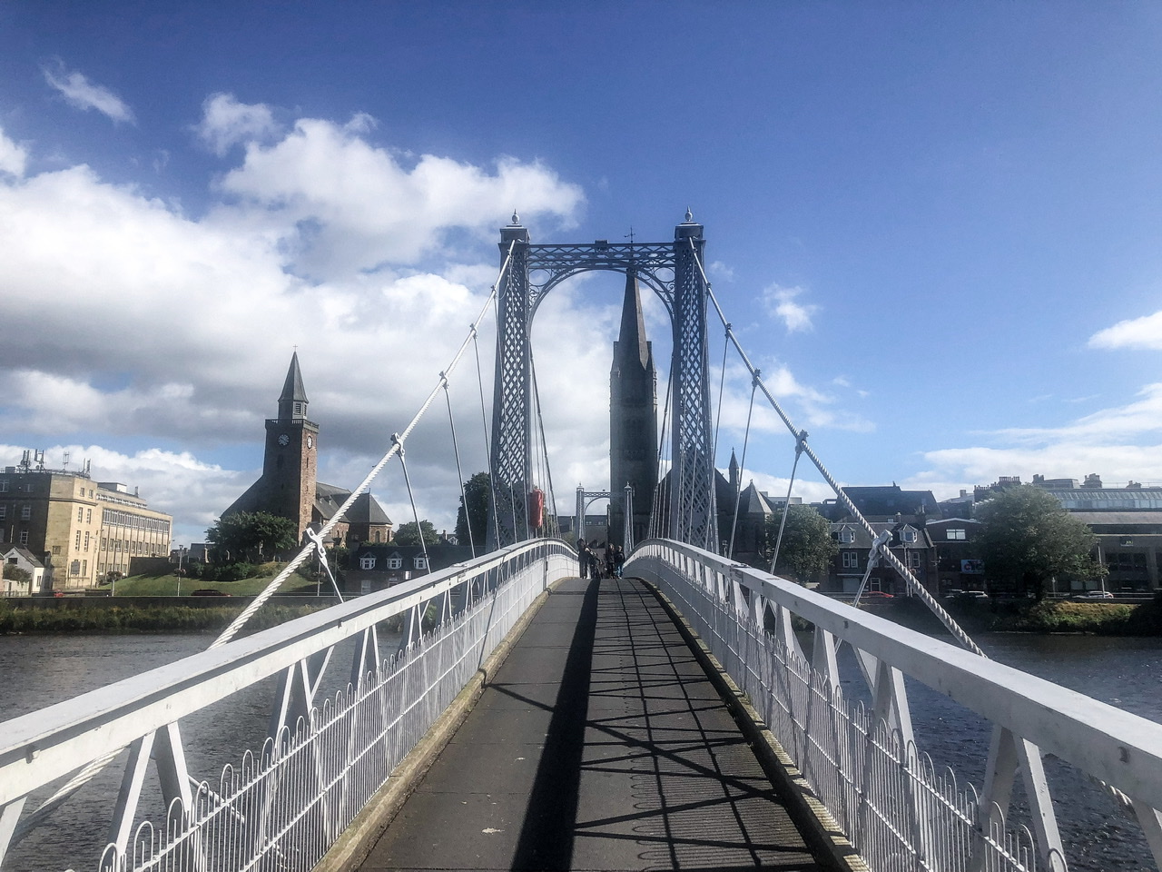 white pedestrian footbridge over a river with church spires visible on far side