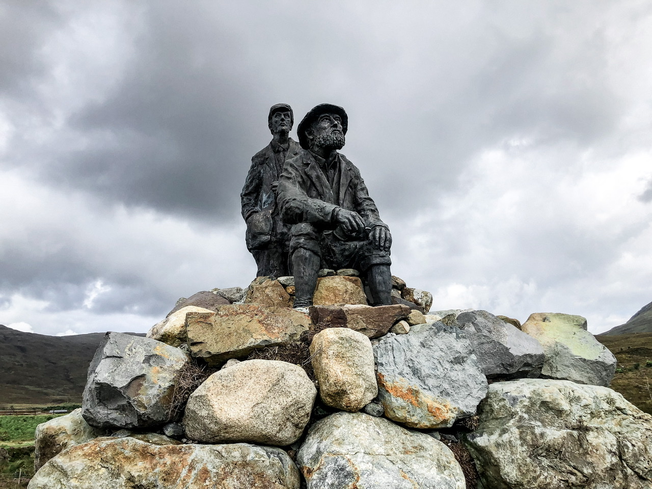 Statue of two explorers, one standing behind a seated one on top of a pile of rocks