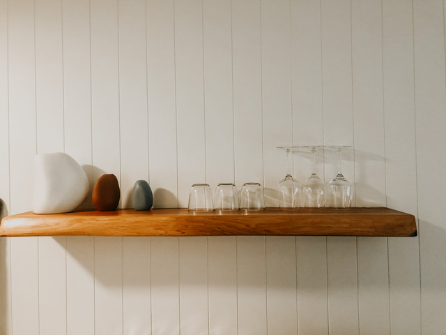 Floating wooden shelf with three coloured vases, three drinking glasses and three wine glasses