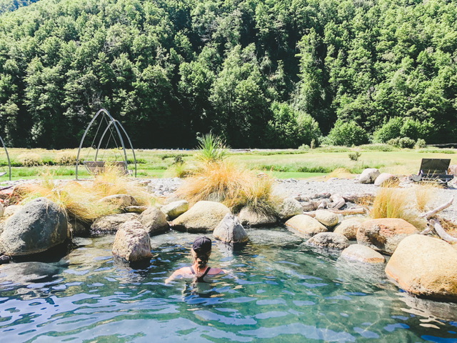 Young woman facing away from camera in outdoor natural hot pool with native bush in background