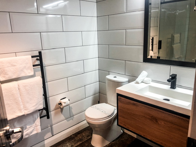 bathroom in chief henshaw apartment hokitika firestation with white towels on black heated towel rail, toilet, basin and mirror above it