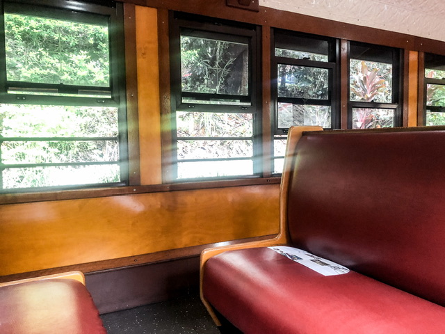 Interior of Kuranda Scenic Railway train carriage with two red leather bench seats facing each other, wooden panelling and windows
