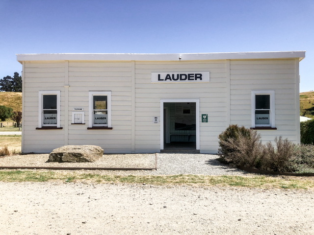 White weatherboard historic railway station buiding with sign reading "LAUDER" above off-centre doorway