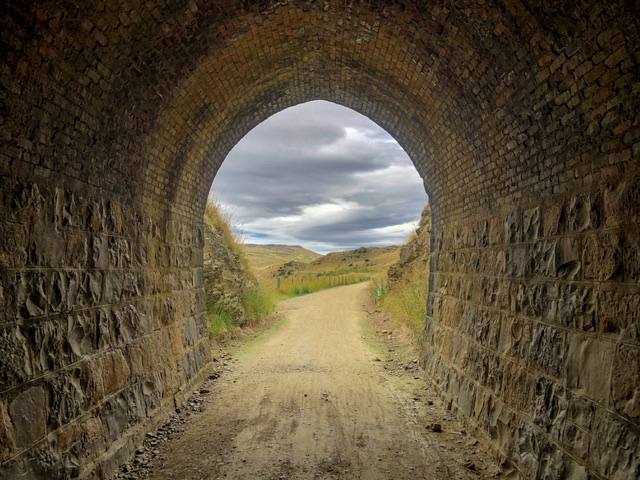 Looking out of an old trail tunnel towards green hills.