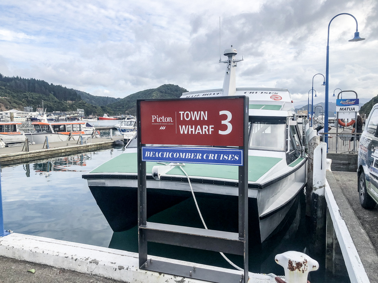 Medium sized boar parked at the end of a marina. Sign in front of it says “Picton Town Wharf 3, Beachcomber Cruises”
