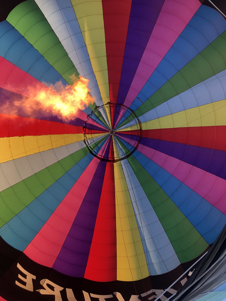 Looking up from hot air balloon basket into colourful inflated hot air balloon. Flames can be seen firing into the balloon.