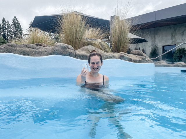 Young woman in black togs drinking wine in Tranquillity Pool at Ōpuke Thermal Pools