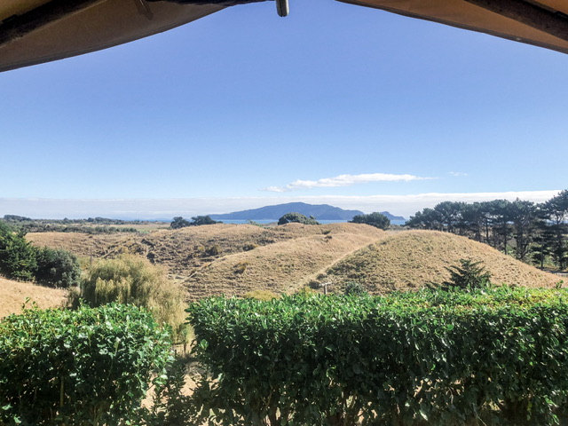 View of Kāpiti Island from Te Hāpua Coastal Glamping balcony. Outlook over green hills and trees to blue sea and Kāpiti Island in the centre.