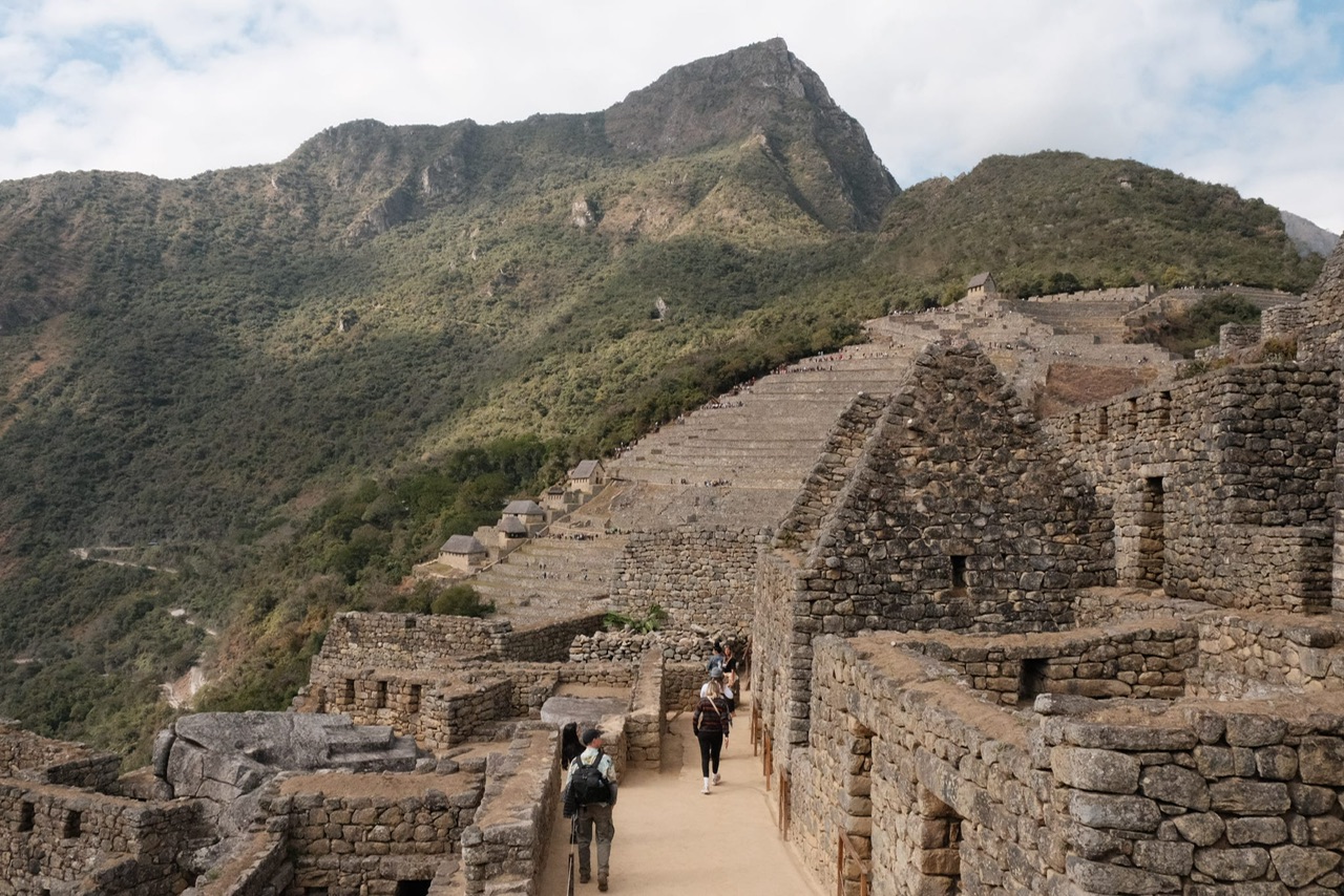 Machu Picchu ruins with mountains in background and a few tourists exploring inside the city.