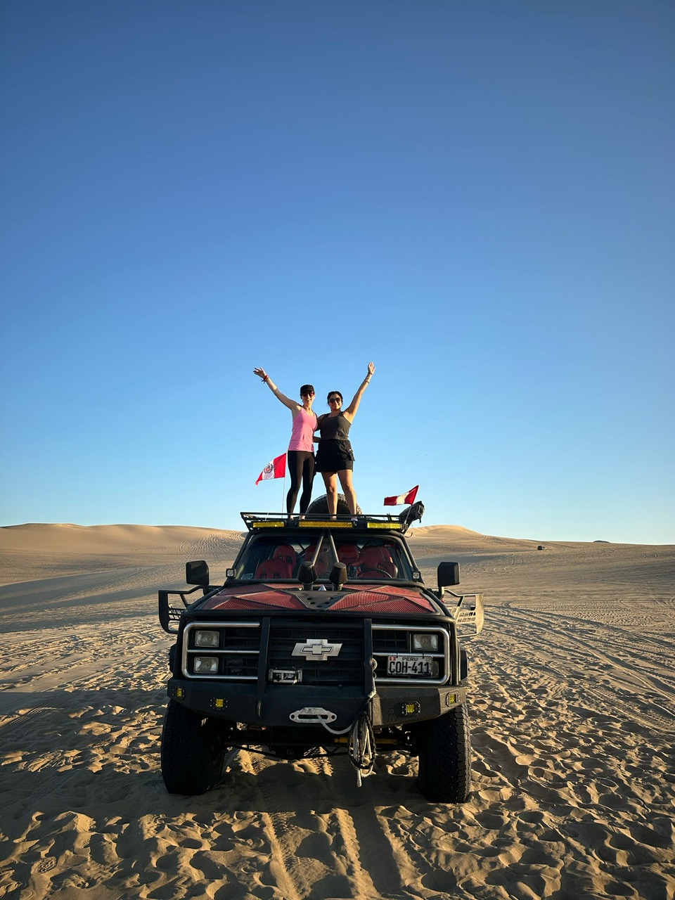 Two young women stand on top of a Dune Buggy in the Huacachina Desert