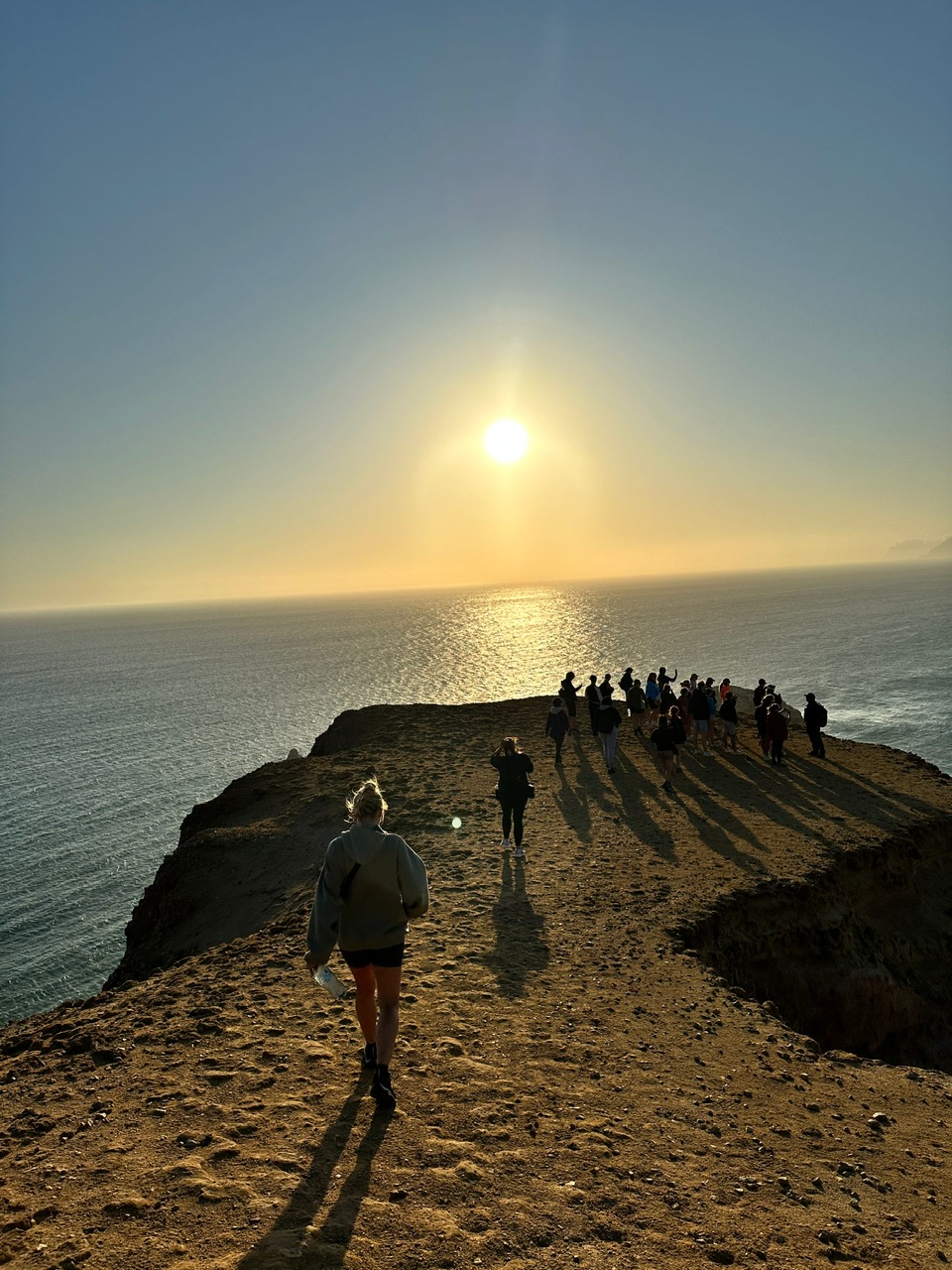 Plotpackers peru group members trek one by one down a cliff face in the Paracas National Reserve at dusk to meet the group.