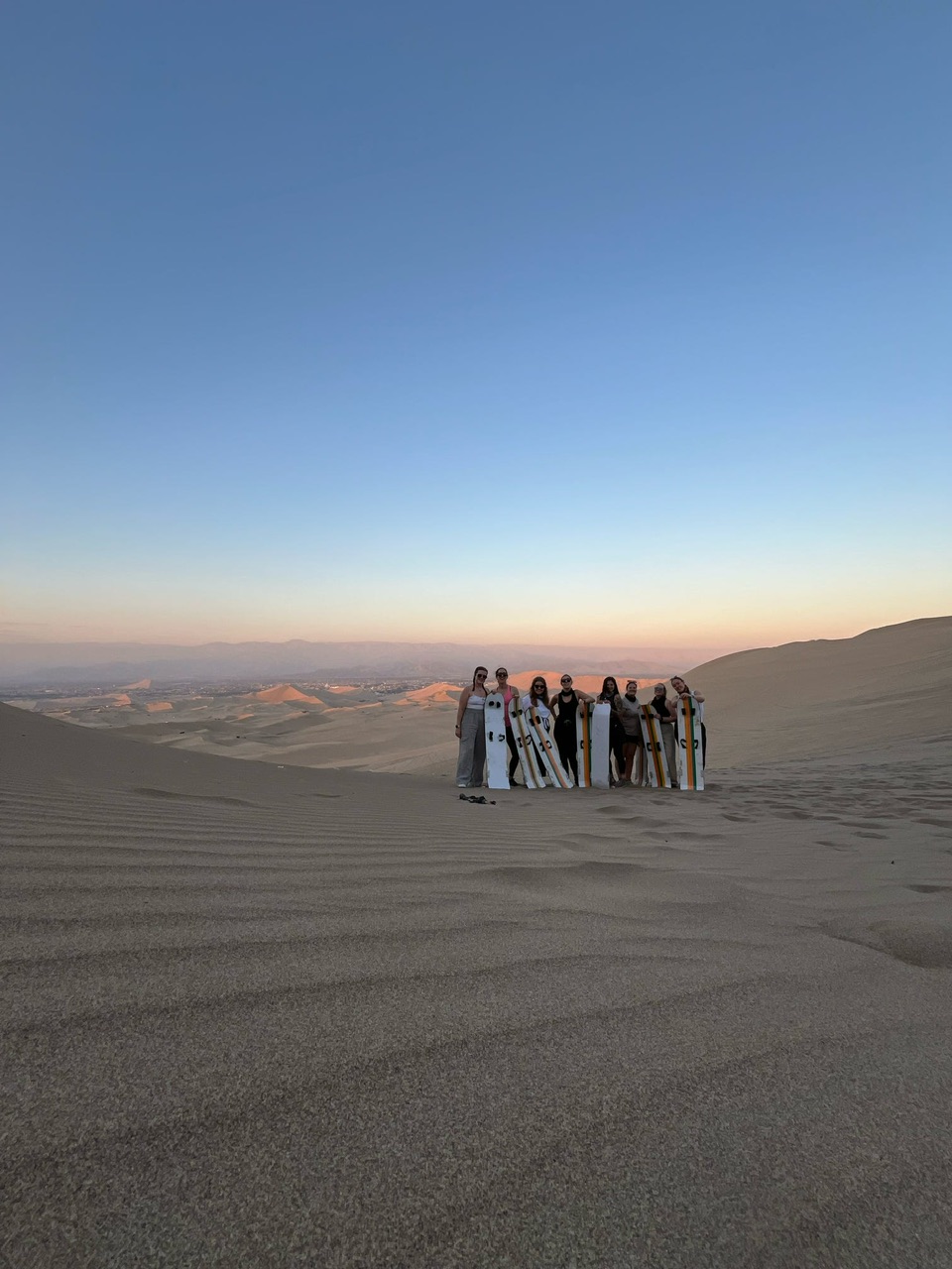 Eight young women stand as a group with sandboards in the Huacachina Desert Peru