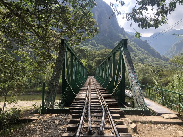 Green railway bridge with pedestrian bridge attached on right over river between hidroelctrica and aguas calientes