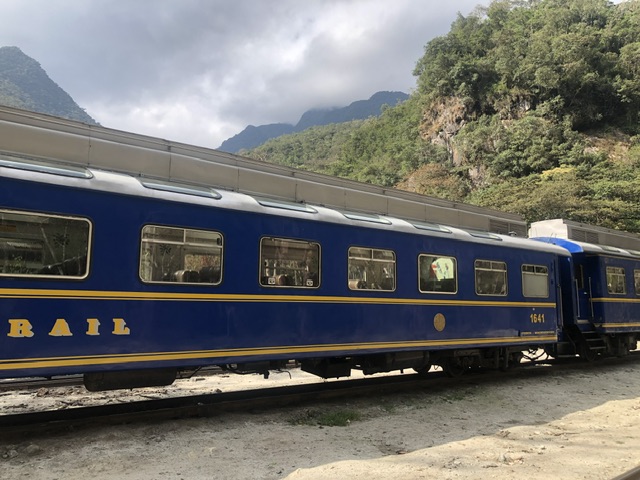 Blue train carriages with mountains and jungle in the background on a grey cloudy day on the walk from Aguas Calientes to Hidroeléctrica.