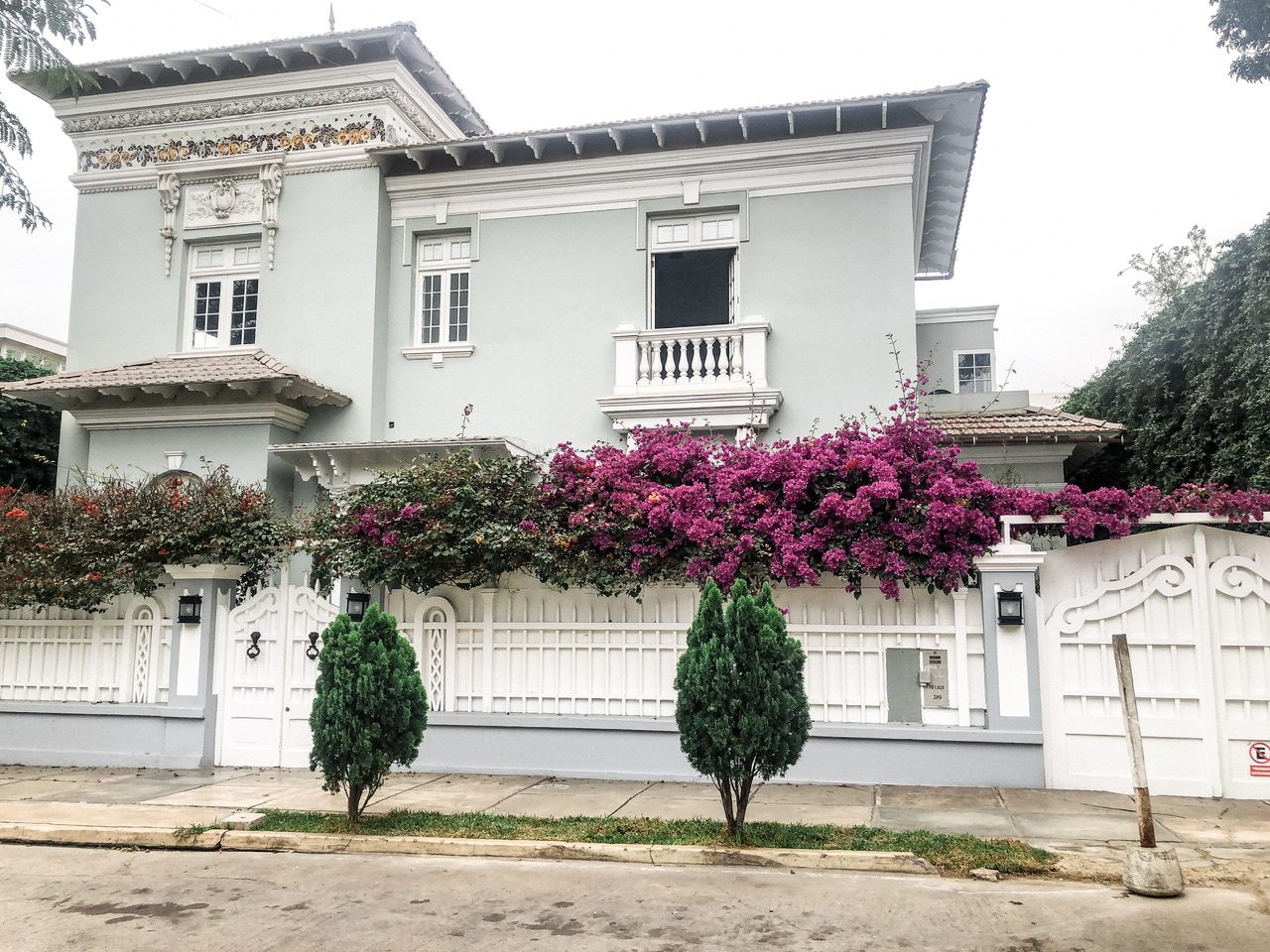 Exterior of a building in Barranco, Lima with manicured bushes and blooming purple flowers along the exterior concrete wall