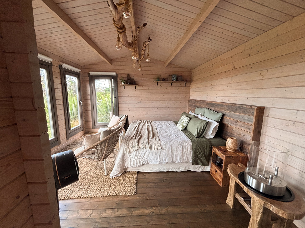 Wahapū Cabin Interior showing bed and chairs looking outside.